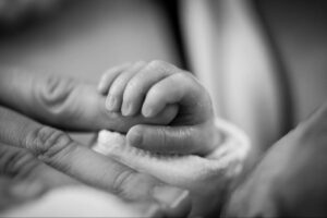 black-and-white image of an infant holding an adult hand.