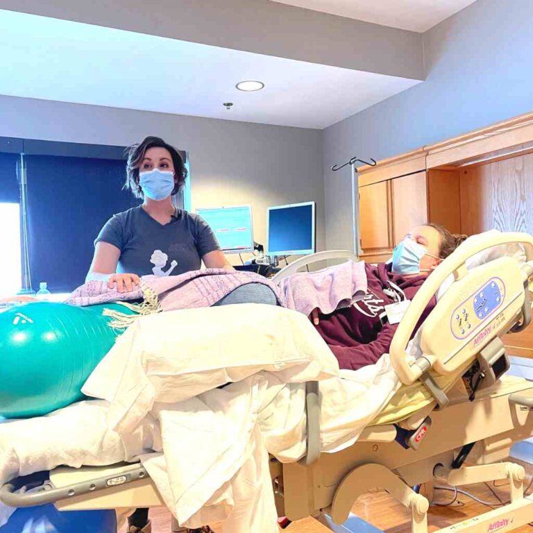 nurse in a mask positions a pregnant person in hospital bed with green peanut ball